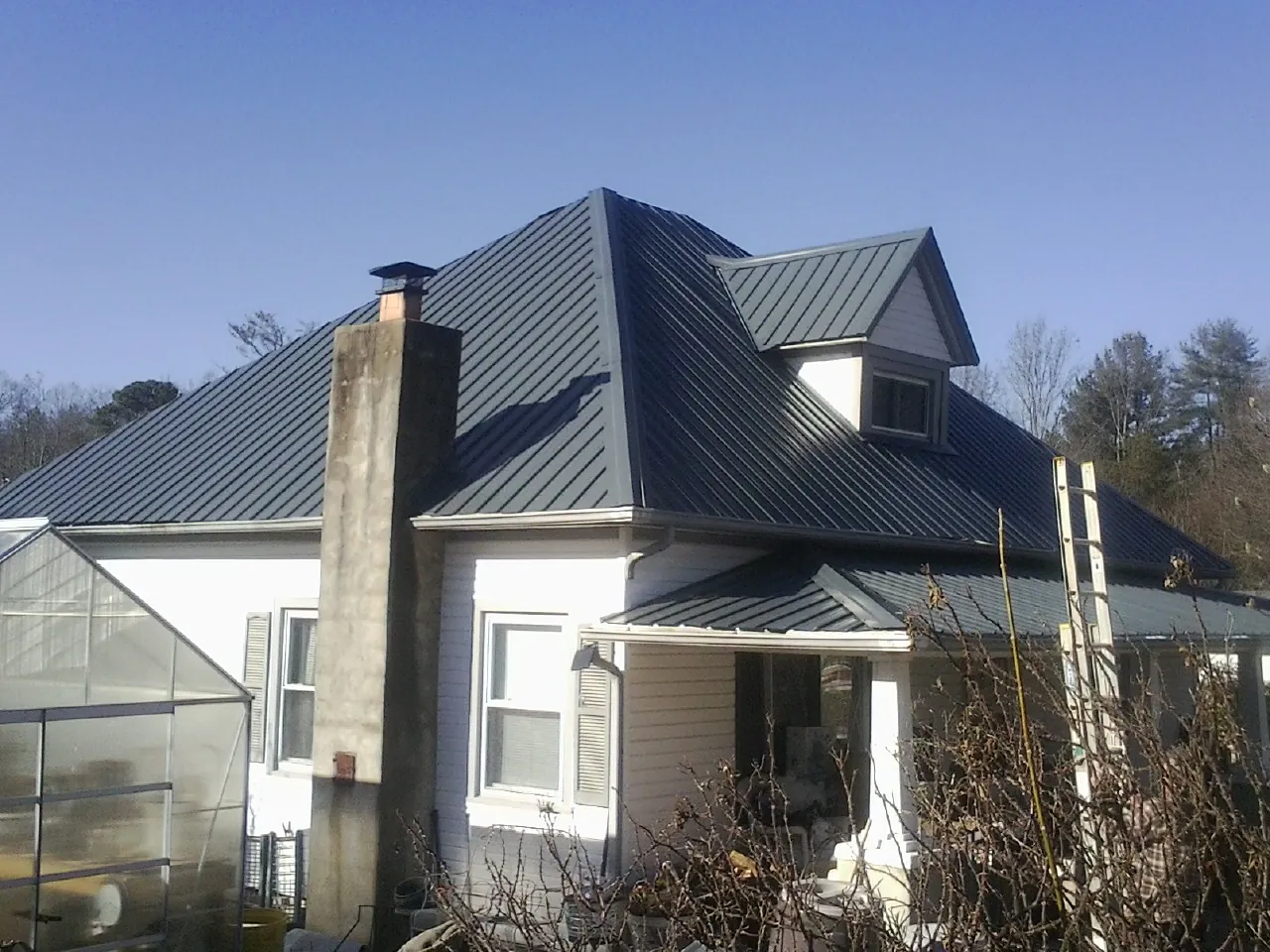 Dark blue standing seam metal roof on a white farmhouse with dormer — Slate & Tile Roof Repair by Roofing Brothers in Swanlake