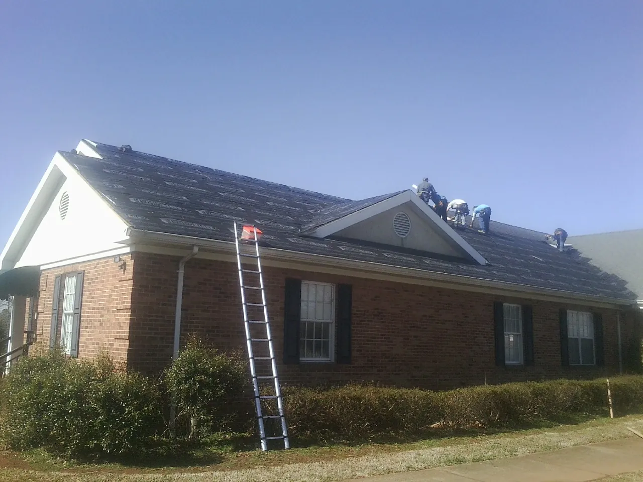 Crew tearing shingles off a brick ranch roof with a ladder set — Emergency Roof Repair work by our crew in Swanlake