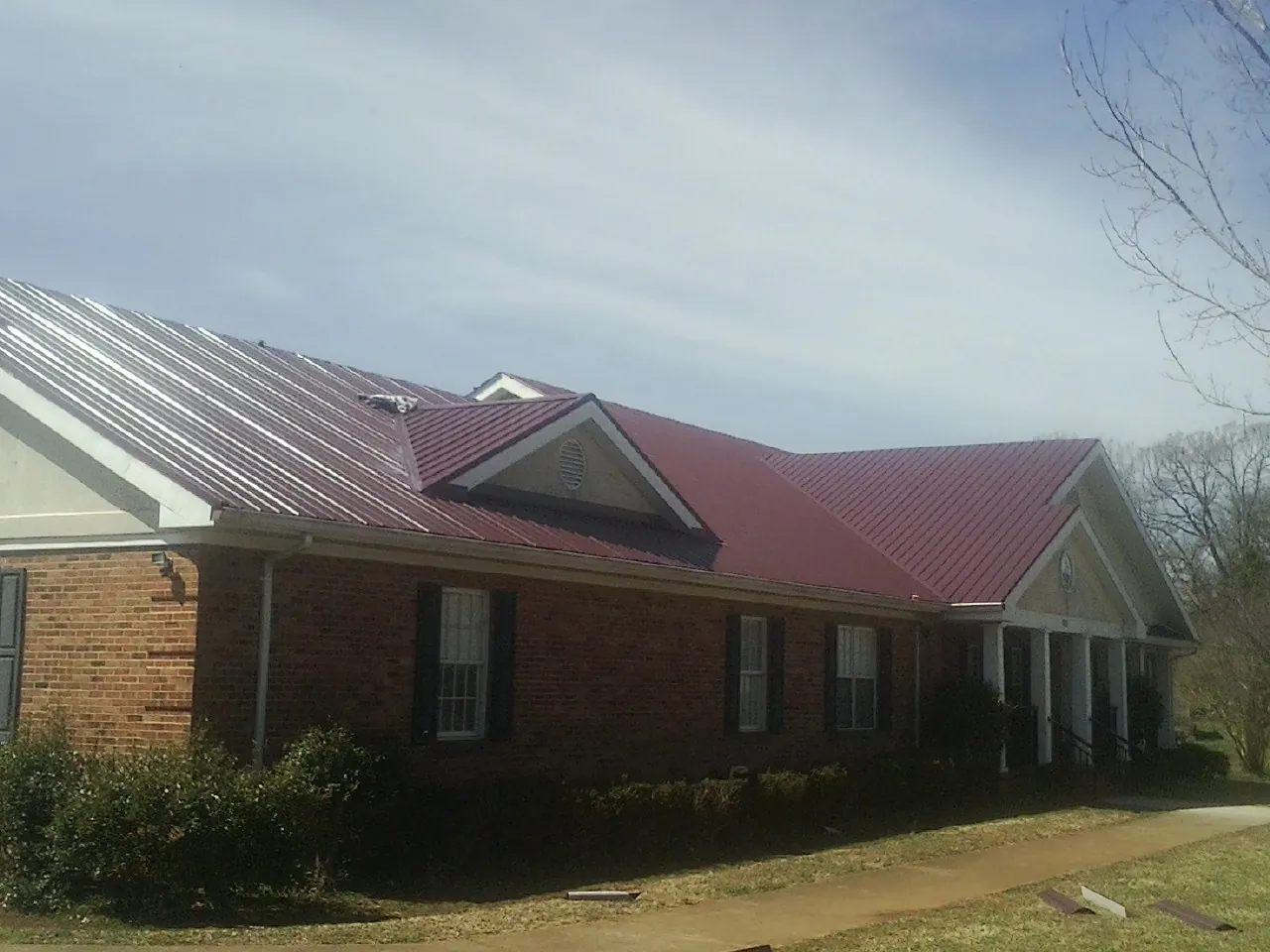 Red metal roof with gabled entries on a long brick building, from a Hail Damage Roof Repair job in Swanlake