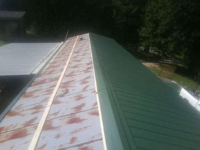 Old rusted panels beside newly installed green metal roofing — Wind Damage Roof Repair by Roofing Brothers in Swanlake