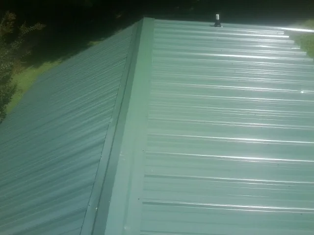 New green metal panels meeting at the ridge of a roof — Flat Roof Repair work by our crew in Swanlake