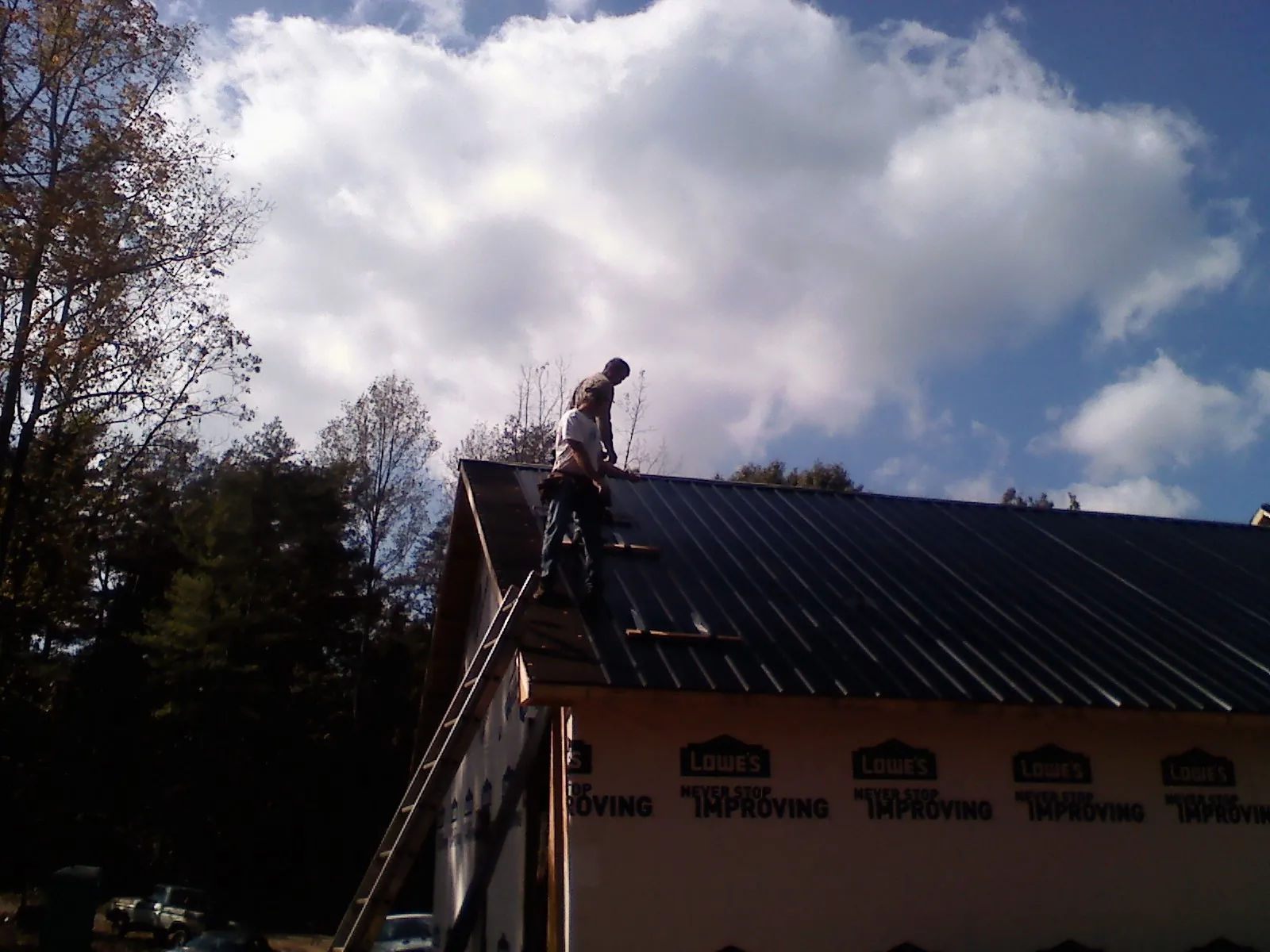 Roofer fastening dark metal panels high against a cloudy sky, from a Roof Inspection job in Swanlake