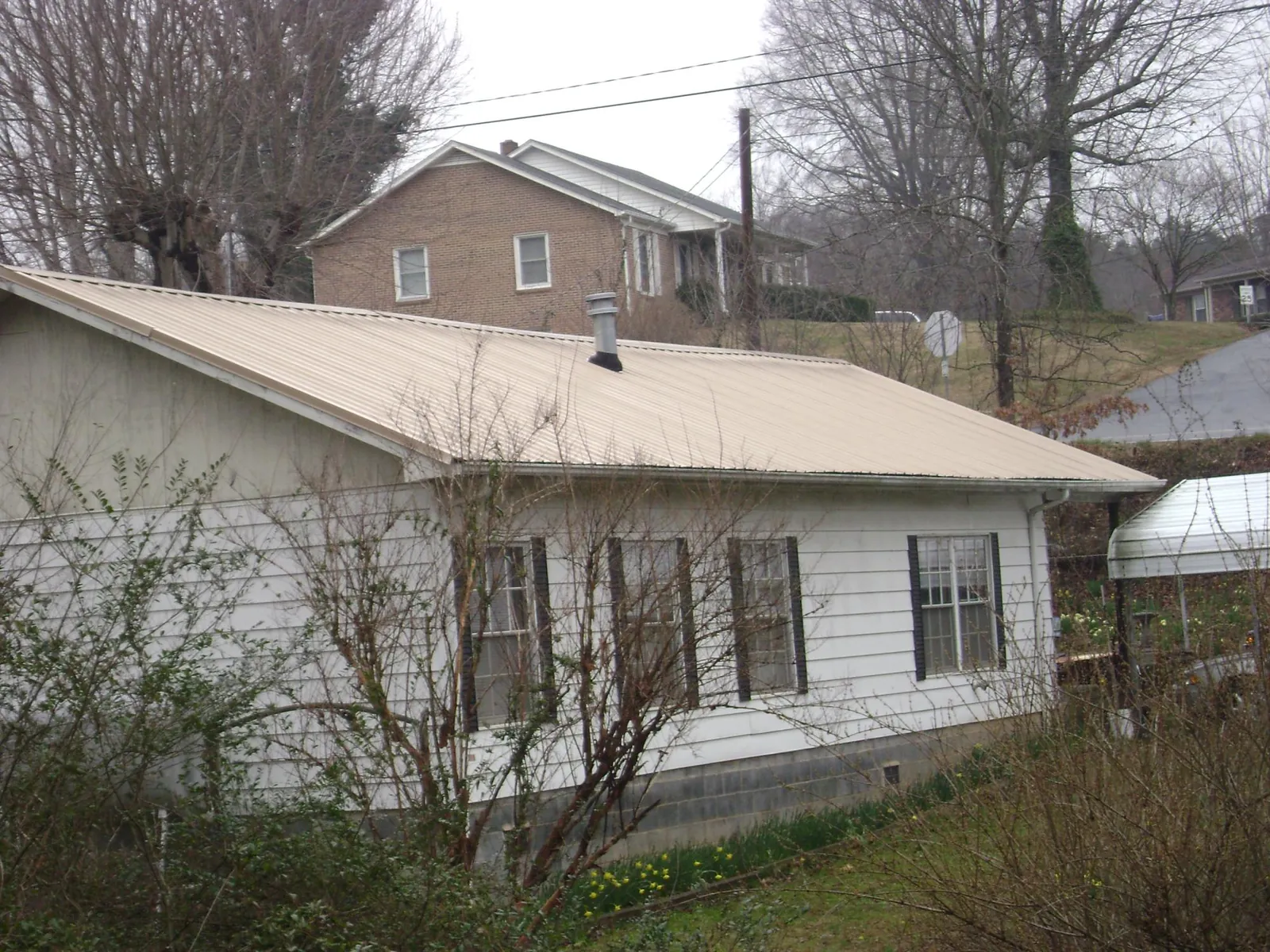 Tan metal roof on a white sided house set into a hillside — Commercial Roofing by Roofing Brothers in Swanlake