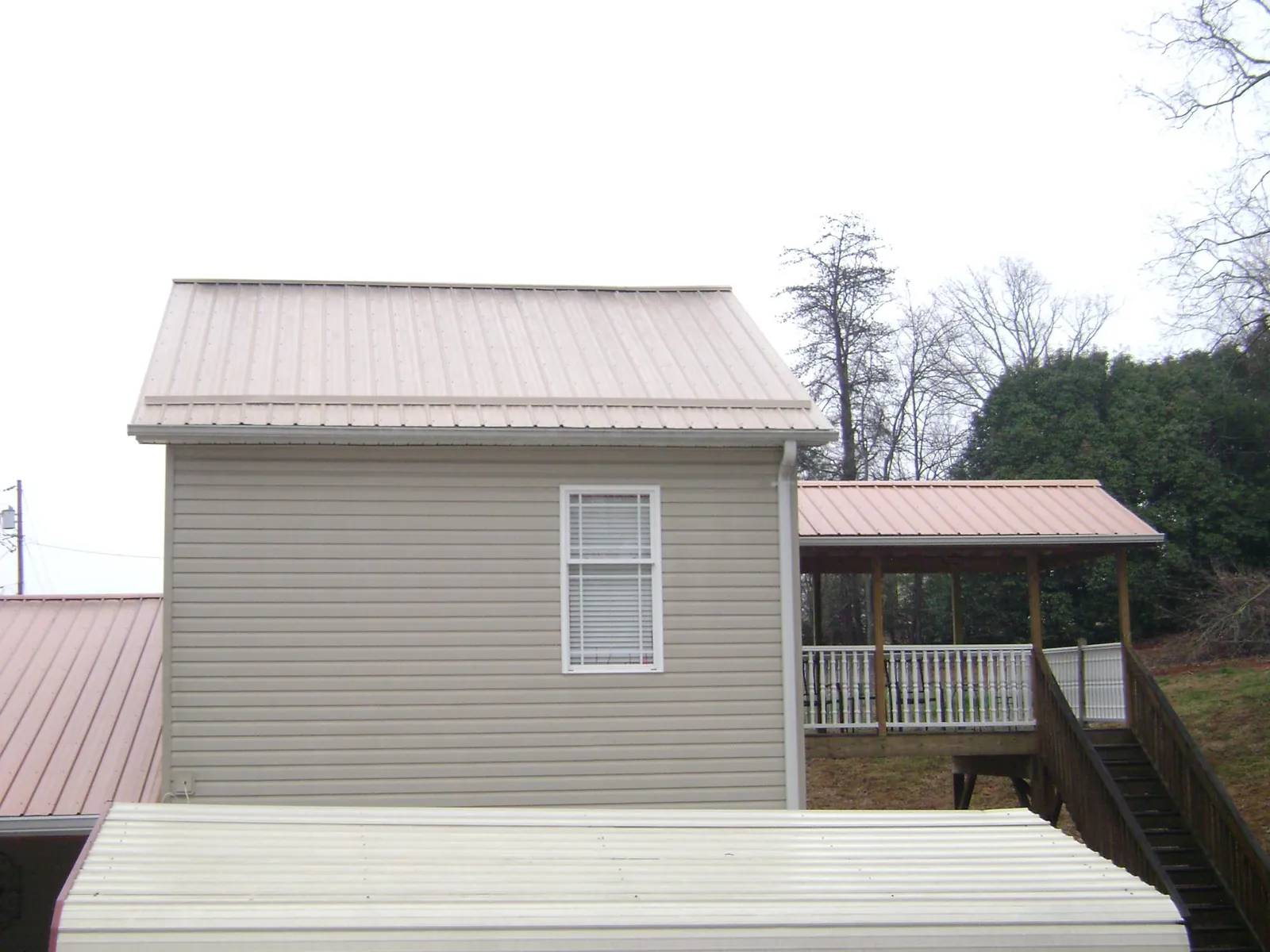 Tan metal roofs on a two story addition and attached porch, from a Roof Replacement job in Swanlake
